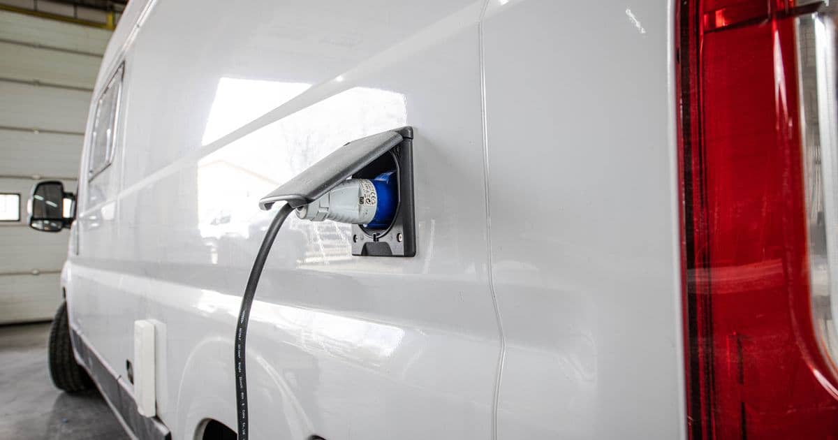 Shore power cable plugged into the inlet on the side of a camper van